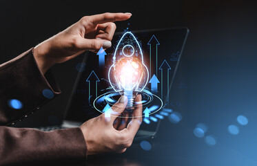 Futuristic rocket startup launch concept with holographic interface held by hands over laptop in dark modern workspace environment background.