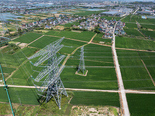 Power transmission towers stand in a vast green field under a clear sky.