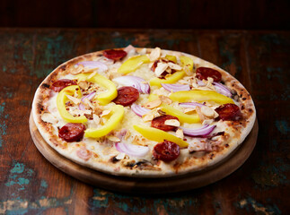 Pizza with chorizo ​​sausage, mozzarella cheese and yellow pepper. Rustic wooden background. Soft focus.	