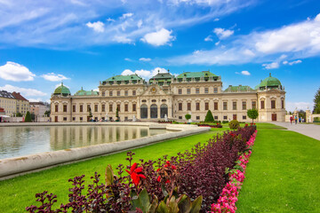 Historic Belvedere palace in Vienna with reflection in the water, green garden and blue sky.