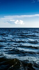 Obraz premium Vast expanse of dark blue ocean meeting a clear blue sky with a single cloud