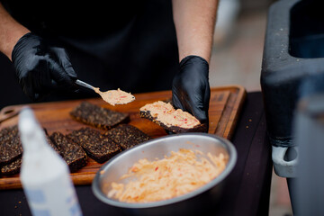 Culinary preparation scene with chef wearing black gloves adding cheese spread to rye bread slices, making traditional appetizer, close up food photography concept