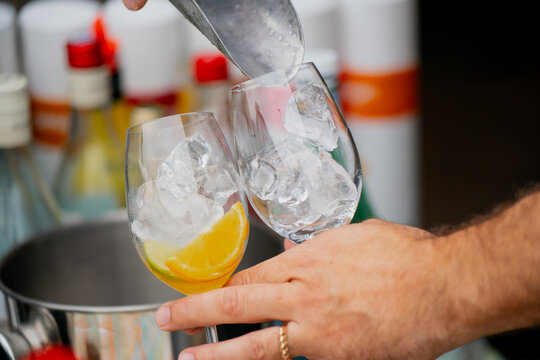 Bartender placing ice cubes into glasses with citrus slice for cocktail preparation, chilled refreshing drink setup for parties, celebrations, summer evenings and gatherings