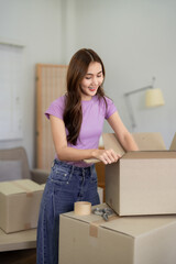 Asian Woman Packing Moving Boxes in New Home Apartment Smiling Young Female Relocating Belongings Happy with House Relocation Moving Day Preparation