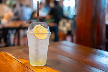 A glass of honey lemon soda on the wooden table, with bokeh background of the restaurant