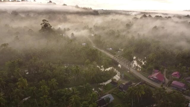 Aerial drone view of Bosua village surrounded by dense forest on Sipora Island, Mentawai, West Sumatra, Indonesia. Morning mist and sunlight create a serene tropical atmosphere.