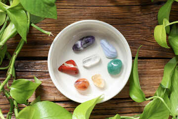 Aura. Different natural mineral stones in bowl and green leaves on wooden table, flat lay