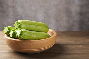 Fresh ripe zucchinis in bowl on wooden table, closeup. Space for text