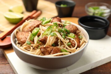 Tasty noodles with chicken, green peppers and sesame seeds served on wooden table, closeup
