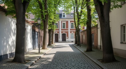 Cobblestone street framed by trees leading to a red brick building with white window trim and doors