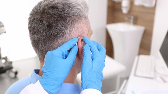 Audiologist installing hearing aid on ear of adult man in hearing clinic. Deafness Treatment, hearing solutions