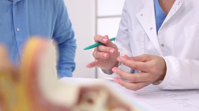 Female audiologist offers behind-the-ear hearing aids to man patient with hearing problems for treatment his deafness. Hearing aids selection