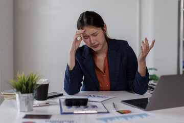 Business asian woman with head in hand at desk in office
