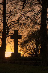 Ancient cross tombstone silhouetted at sunset