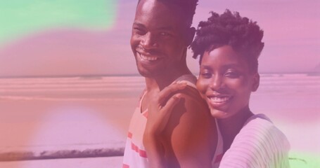 Smiling romantic couple wearing striped tops standing close on sandy beach, dreamy pastel overlay