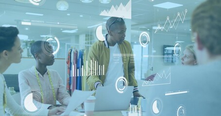 Presenting man in mustard bomber at workspace, with laptop, tape, garment racks and data overlays