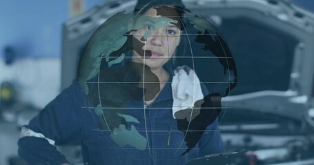 Mechanic scanning engine under hood in bay, wearing coveralls and holding tablet with globe overlay