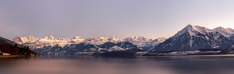 Idyllic swiss lake and landscape at dawn. Panoramic view of lake thun with surrounding swiss alpine landscape with snow capped mountains