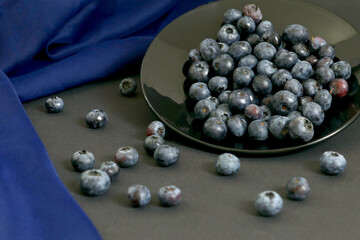 Blueberry still life on black plate with dark background and blue fabric