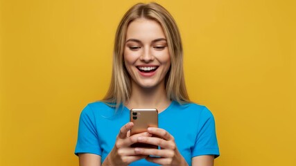 Young woman texting on smartphone in front of a yellow backdrop, smiling and looking down at her phone, social media concept, video - Powered by Adobe