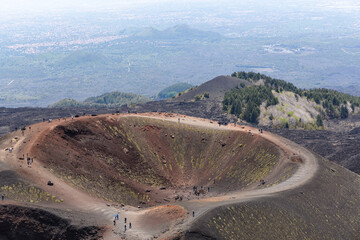 Aerial view of a volcanic crater with people walking along its rim, surrounded by rugged terrain...