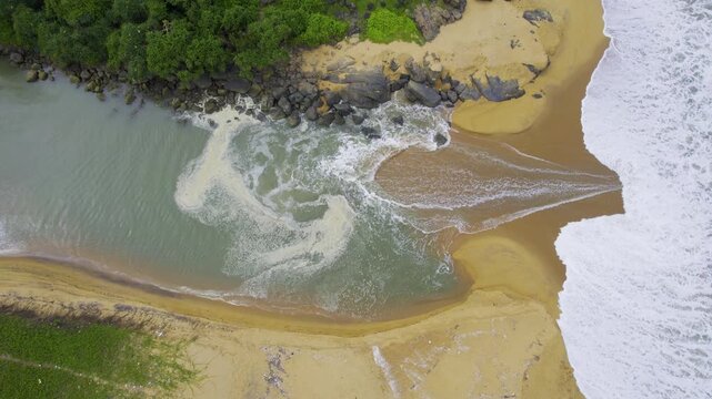 aerial drone shot straight down showing waves pushing water into backwater inlet in Kappil bekal beach with rocks to the side and blue green water showing the beauty of god's own country Kerela