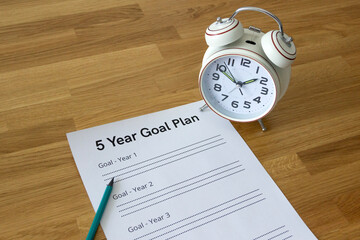 sheet '5 Year Goal Plan' with an alarm clock standing on it on a wooden table