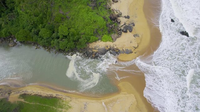 aerial drone shot rising straight down showing waves pushing water into backwater inlet in Kappil bekal beach with rocks to the side and blue green water showing the beauty of god's own country Kerela