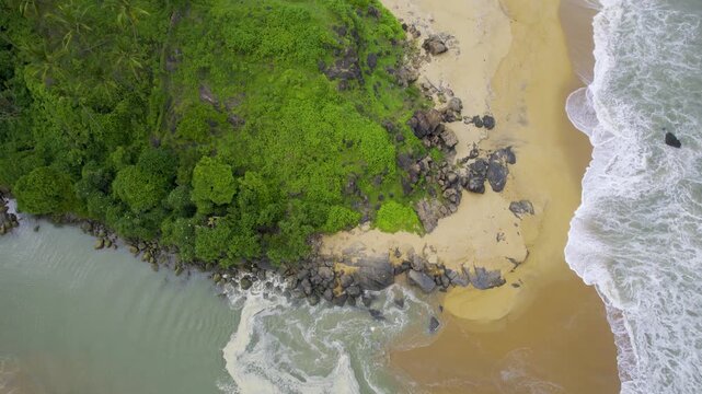 Aerial drone shot panning up from backwater inlet on kappil beach to green tree and bush covered coastline and golden sand beach with waves crashing into it