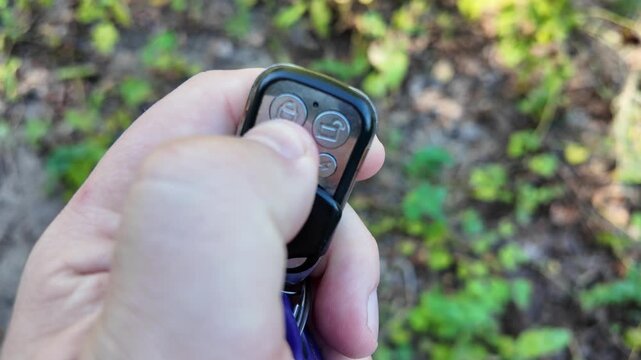 In a man's hand the alarm key fob, when the button is pressed, a red LED lights up, signaling that the protected object has been alarmed. Closeup.