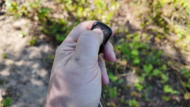 In a man's hand the alarm key fob, when the button is pressed, a red LED lights up, signaling that the protected object has been alarmed. Closeup.