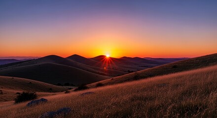 Obraz premium Sunset between rolling hills with radiant sunbeams over a grassy landscape