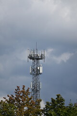 Lattice mast with 5G antennas between houses, light clouds in the sky
