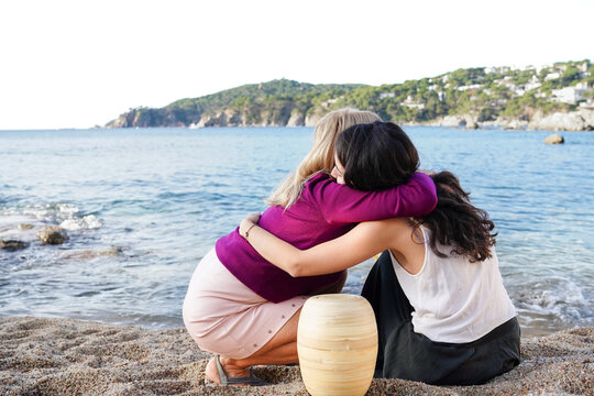 Mother and daughter embrace with ashes by the seaside