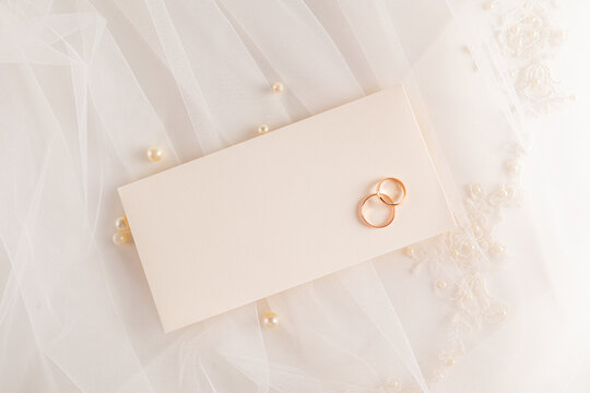 Elegant wedding rings on beige envelope with lace veil