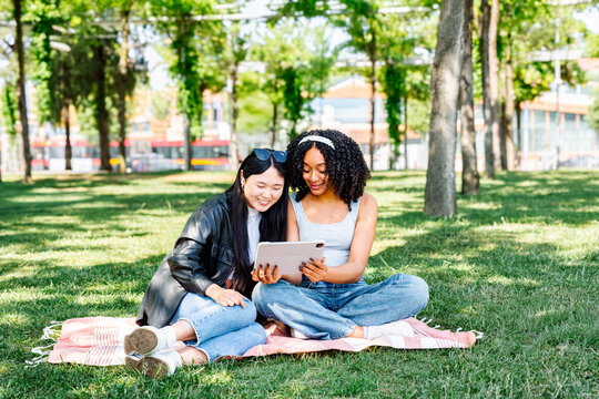 Friends enjoying a sunny day in the park looking at a digital tablet