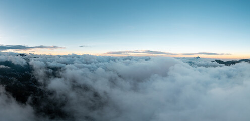 Aerial view above the clouds at sunset, with golden light illuminating soft white and gray layers, creating a serene and peaceful atmosphere high in the sky.
