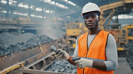Industrial engineer wearing safety gear is assessing the quality of coal inside a large processing plant, highlighting the importance of quality control in heavy industries