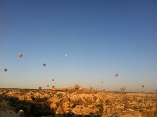 Hot Air Balloons and Moon Over Rocky Landscape at Sunrise in Cappadocia, Turkey