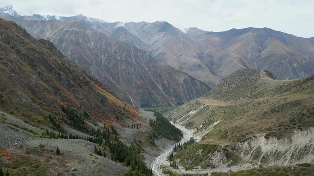 Autumn view of mountains and river in Ala Archa National Park, Kyrgyzstan, with golden and rocky slopes.