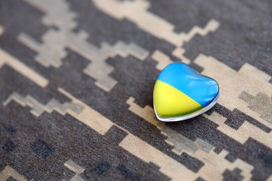 Glass heart with Ukrainian flag lies on military camouflage fabric. Concept of support Ukraine