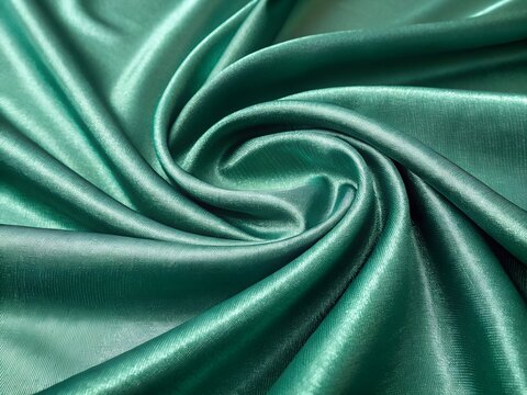 Green satin fabric draped in elegant swirling folds