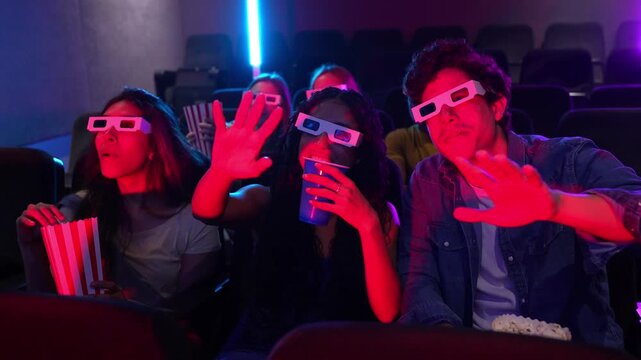Young people wearing 3d glasses watch a movie at the cinema, eating popcorn and drinking soda, enjoying the show in slow motion