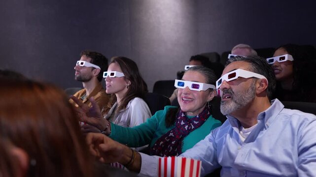People wearing 3d glasses enjoy a movie at the cinema, reacting with enthusiasm and pointing at the screen in slow motion