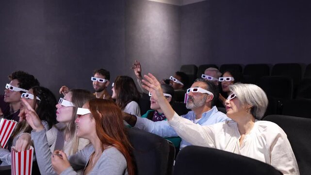 Spectators wearing 3d glasses enjoying a movie at the cinema, pointing at the screen and eating popcorn, in slow motion