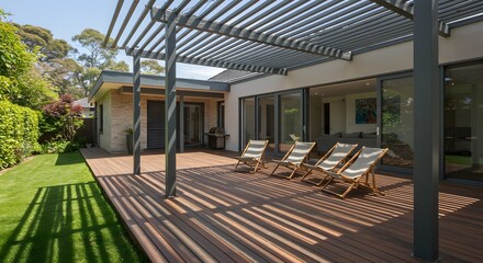 Outdoor space features a pergola casting shadows on a wooden deck with chairs adjoining a lawn and building