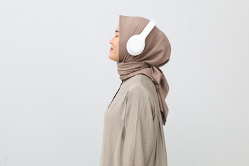 Side profile view young smiling happy Asian muslim woman listen to music in headphones close up isolated on white background studio portrait. Lifestyle concept.