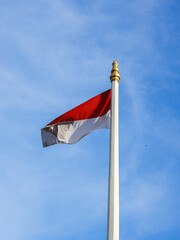 ndonesian red and white flag waving on tall pole against blue sky background