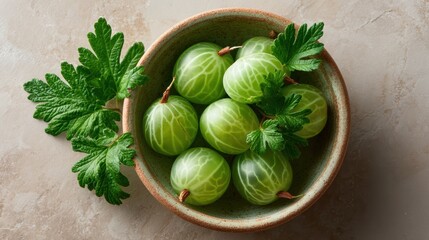 Top-down view of fresh green gooseberries in ceramic bowl with leaves on textured beige background.