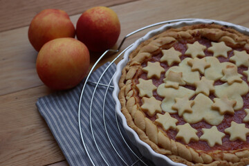 Close-up of homemade peach pie or tart on gray and white striped napkin on wooden table with peach fruits